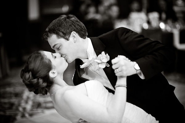 Black and white photo - Groom dipping and kissing bride during their first dance at the reception - photo by Houston based wedding photographer Adam Nyholt